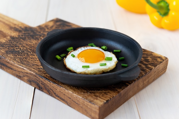 Photo fried egg with green onions in a cast iron skillet and with sweet peppers on a wooden table