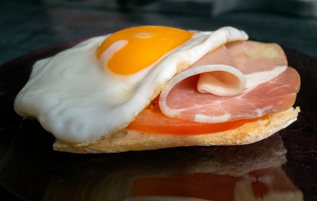 Fried egg with ham and tomatoes on dark plate