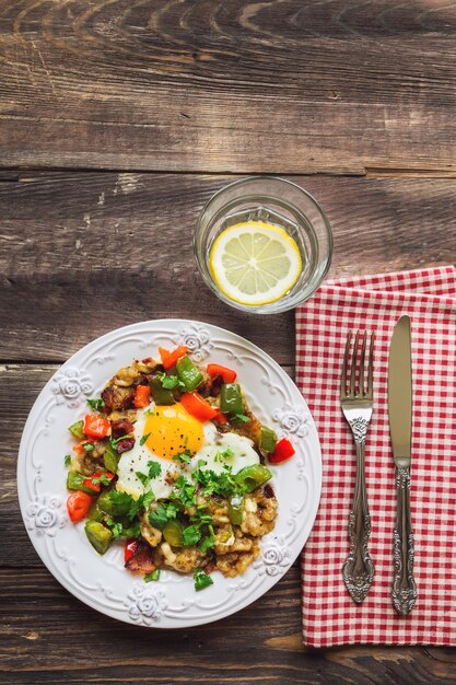 Fried egg with pepper, bacon, potatoes and cilantro on rustic wooden table. Top view.