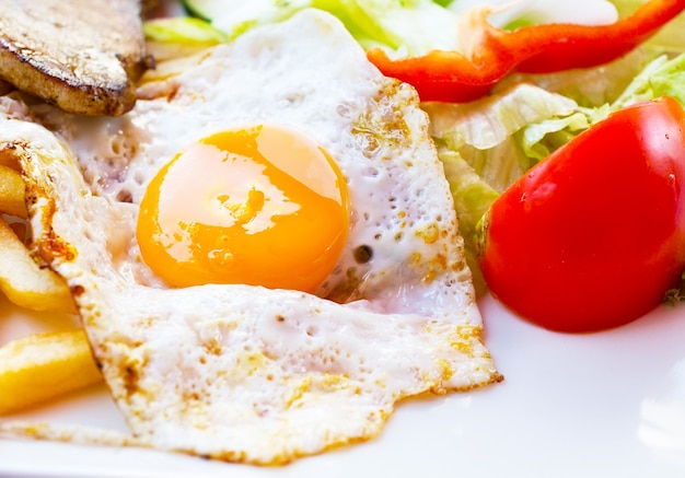 Fried egg with potato fries, grilled steak and vegetables.