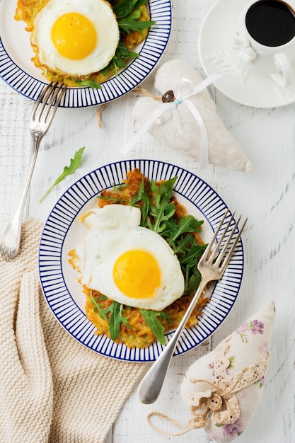감자 팬케이크, arugula, 흰색 나무 테이블 배경에 아침 식사를 위해 세라믹 접시에 아보카도와 튀긴 계란. 평면도.