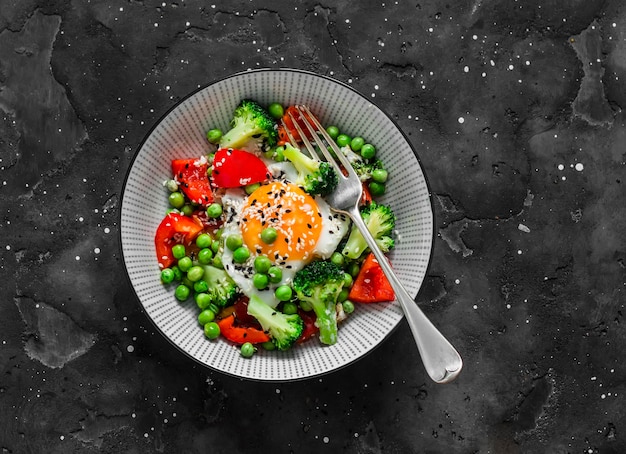 Fried egg with seasonal vegetables for breakfast lunch snack on a dark background top view