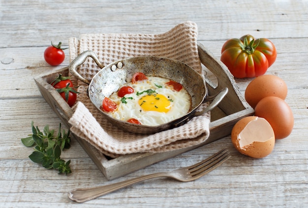 Fried egg with tomatoes and herbs on a old frying pan on wood