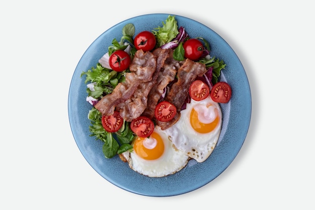 Fried eggs on blue plate with bacon lettuce and cherry tomatoes