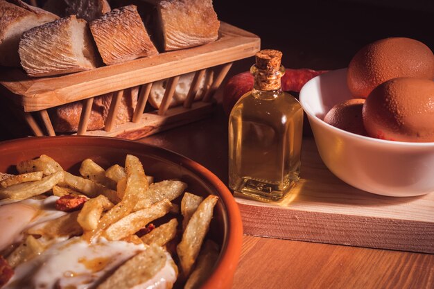 Uova fritte, patatine fritte, olio d'oliva e pane su un tavolo di legno