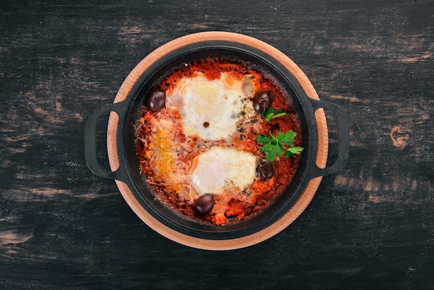 Fried eggs fried in a pan with vegetables and parmesan cheese. On a wooden background. Top view. Copy space.