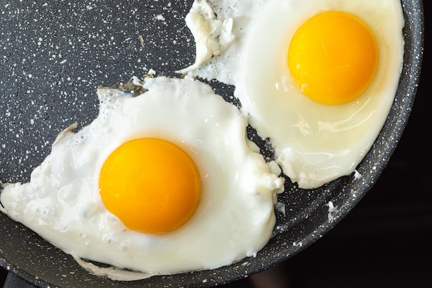 Fried eggs in a frying pan on electric stove top view