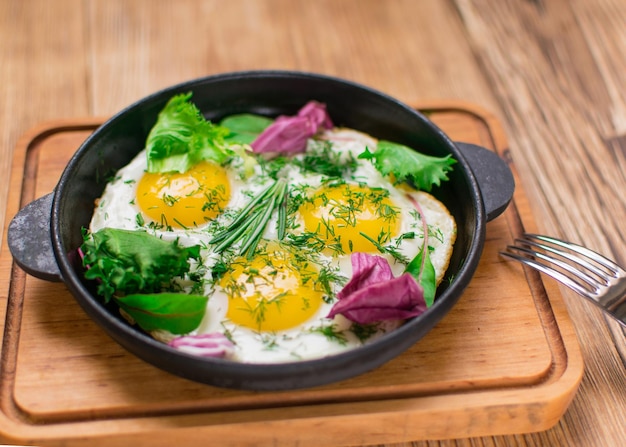 Fried eggs in a frying pan and greens