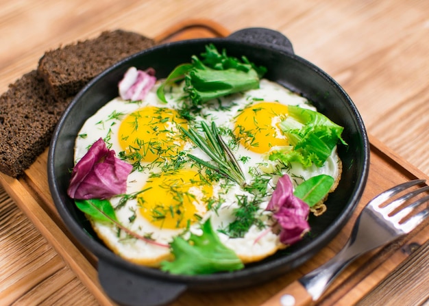 Fried eggs in a frying pan and greens