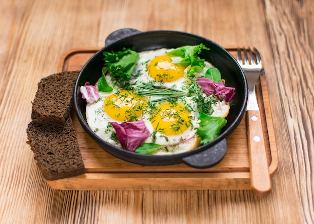 Fried eggs in a frying pan and greens