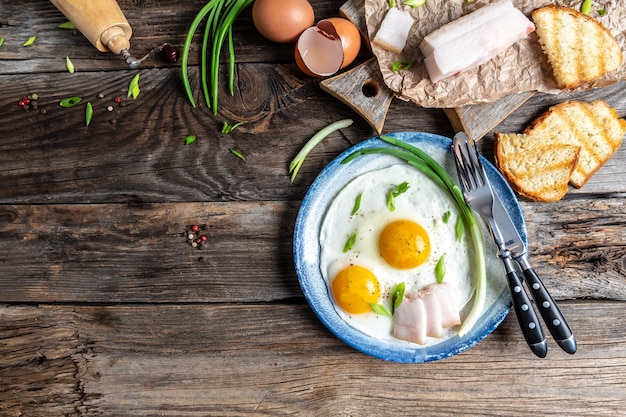 Fried eggs in frying pan with pork lard, bread and green feathers onions