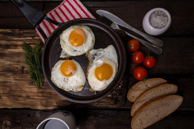 Жареные яйца на сковородке с овощами и травами на черном фоне