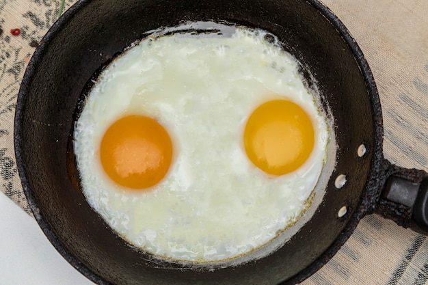 Fried eggs in a rustic iron pan for breakfast. Top view.