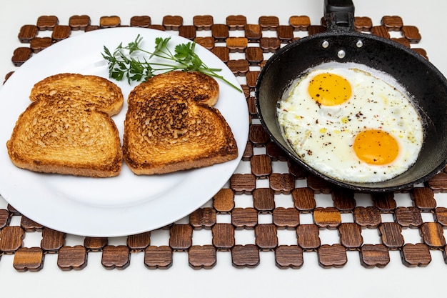 Fried eggs in a rustic iron pan, toast on a dish for breakfast