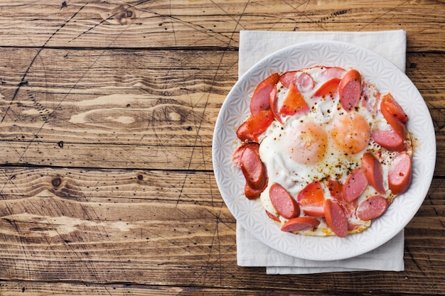 Fried eggs sausages and tomatoes on a plate on the table. 