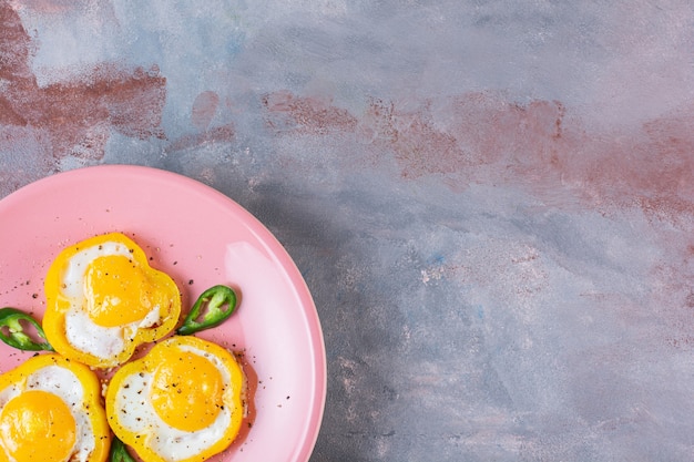 Fried eggs in slices of yellow bell peppers on stone table.