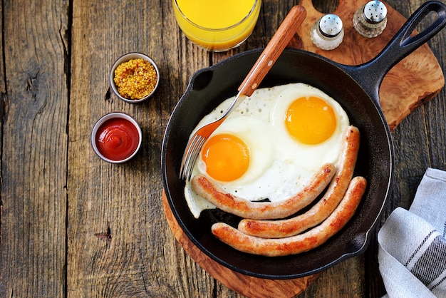 Fried eggs and thin sausages in a cast iron skillet