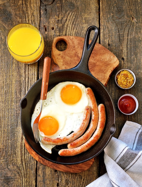 Fried eggs and thin sausages in a cast iron skillet