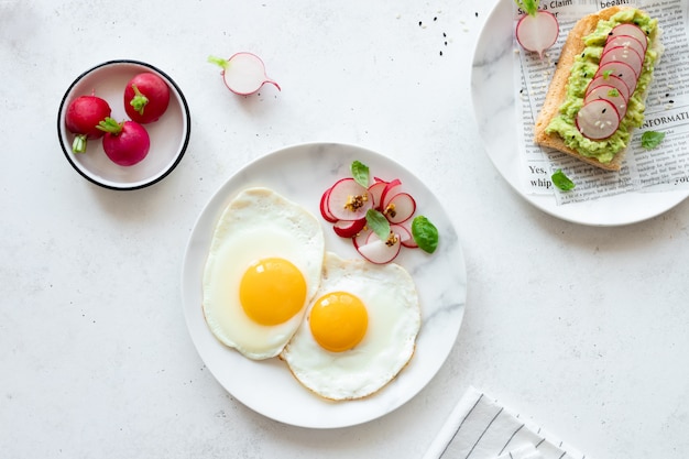 Fried eggs and toast with avocado on plates