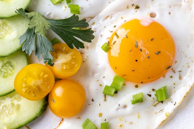 Fried eggs vegetables on a white plate on a white wooden background.