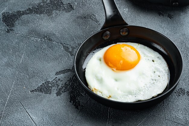 Fried eggs with cherry tomatoe and bread for breakfast in cast iron frying pan, on gray