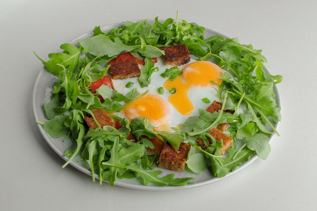 Fried eggs with greens and croutons on a white plate on a white background