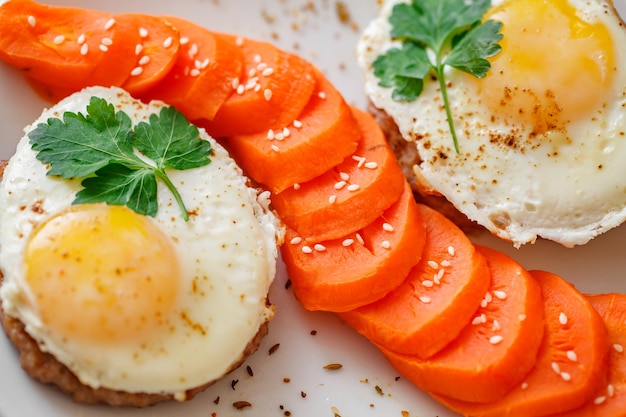 Fried eggs with meat cutlets and carrots with spices and sesame seeds top view closeup selective focus