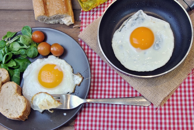 Uova fritte con piatto, pane e oliatore su un tavolo di legno