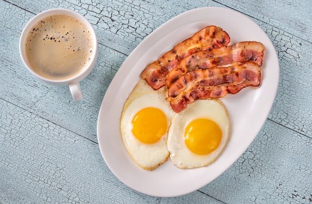 Fried eggs with strips of bacon on the white plate