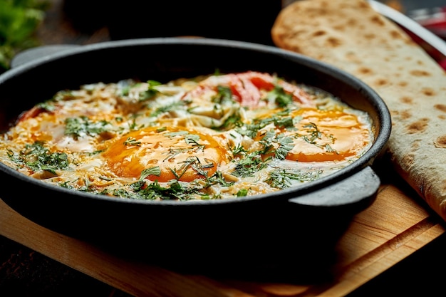 Fried eggs with tomatoes onions and pita bread in a pan on a wooden background Tasty Shakshuka