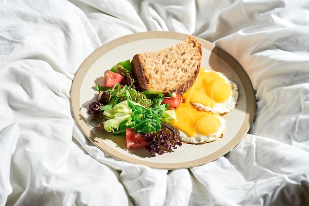 Fried eggs with vegetable salad and cheese in a plate on a white sheet Hard light