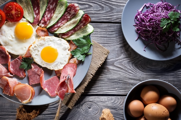 Fried eggs with vegetables and bacon on a wooden table