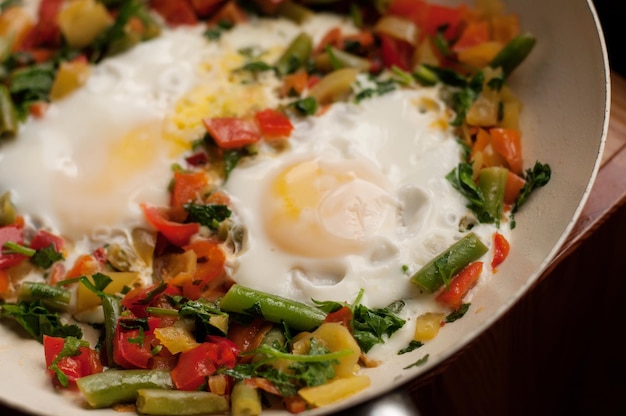 Fried eggs with vegetables in a frying pan