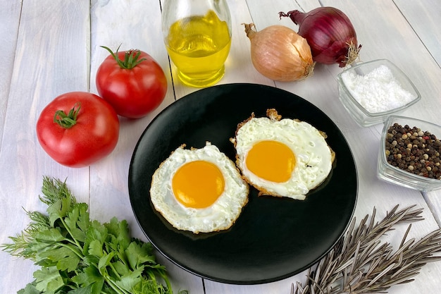 Жареные яйца с овощами, специями и травами на светлом деревянном фоне