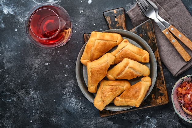 Fried empanadas with cilantro, meat, egg, tomato and chili sauce on black background. Chilean typical dish. Latin American and Chilean independence day concept.