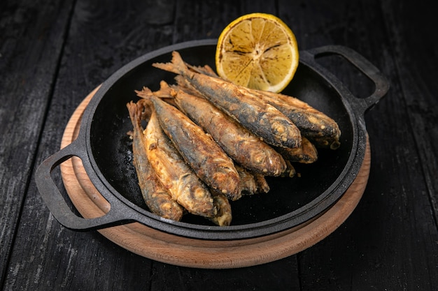 Fried fish on a black cast iron skillet on a dark wooden table