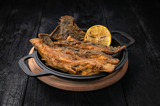 Fried fish on a black cast iron skillet on a dark wooden table