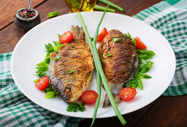 Fried fish carp and fresh vegetable salad on wooden background. 