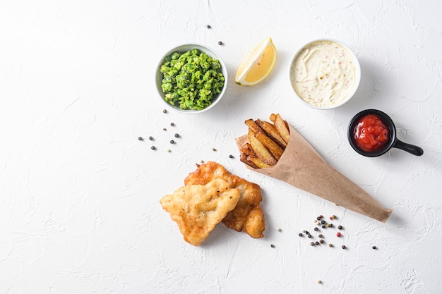 Fried fish and chips in a paper cone on white background with all components classic recipe