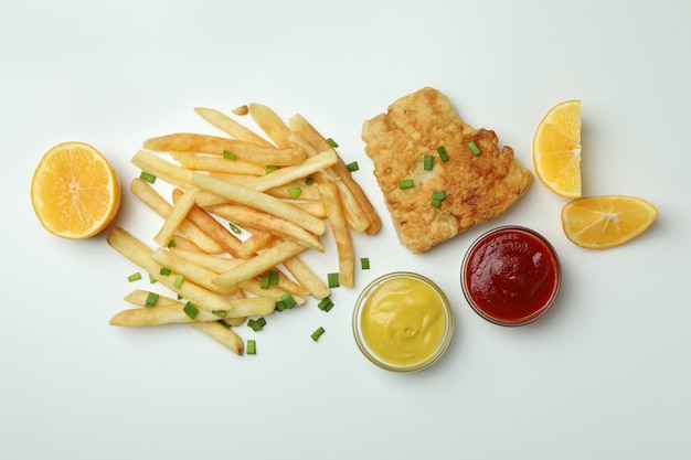 Fried fish and chips, sauces and lemon on white