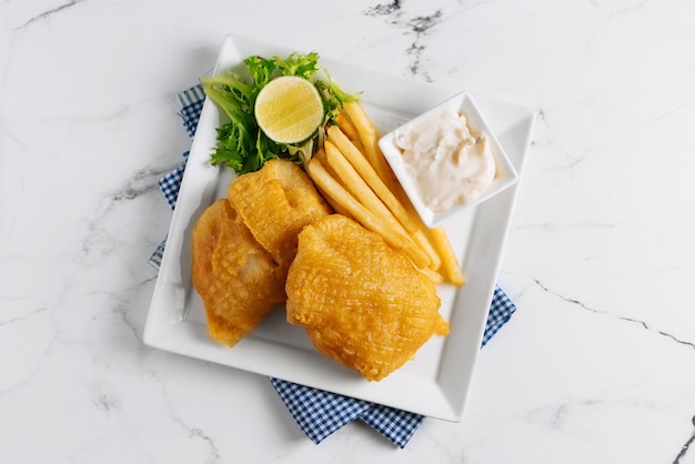 Fried Fish and Chips with lime in a dish basket isolated on napkin side view on grey background famous indian and pakistani food