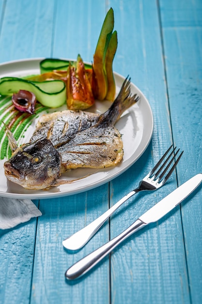 Fried fish dorado decorated with cucumbers and onions on a blue wooden background