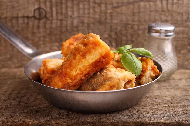 Fried fish hake in a frying pan decorated with basil