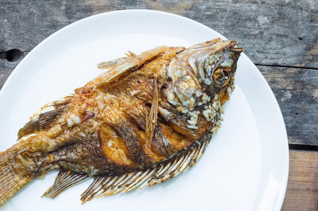 Fried fish Tilapia on white dish on wooden backgroundthai food style