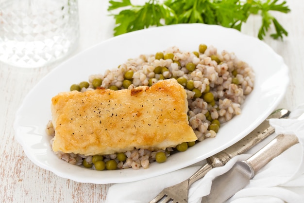 Fried fish with boiled buckwheat and peas in white dish