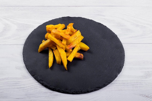 Fried French fries on a black slate plate wooden background