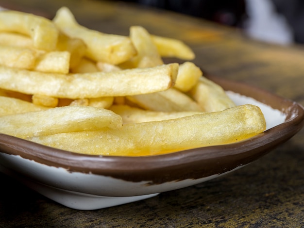 Fried French fries on a white plate with brown border on the wooden table