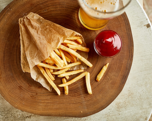 Fried french potato, served on wood with glass of beer and ketchup