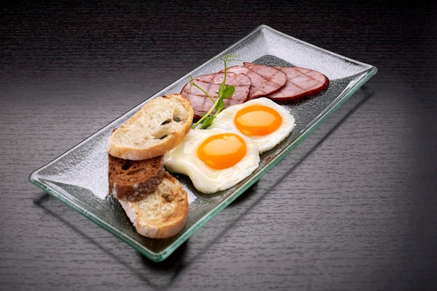 Fried fried eggs with tomatoes, ham and ciabatta toast, on a dark surface. Breakfast