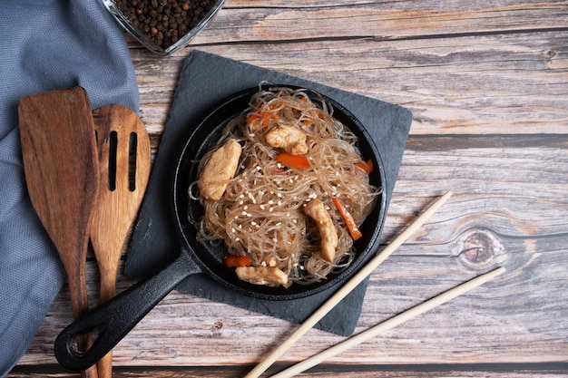 Photo fried funchosa in a frying pan with chicken on a wooden background